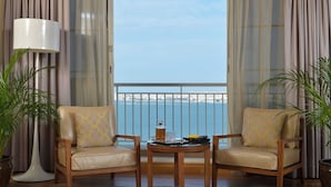 A room with two chairs, a table, a lamp, and a view of the sea. - Mysk Al Fateh Bahrain (Manama)