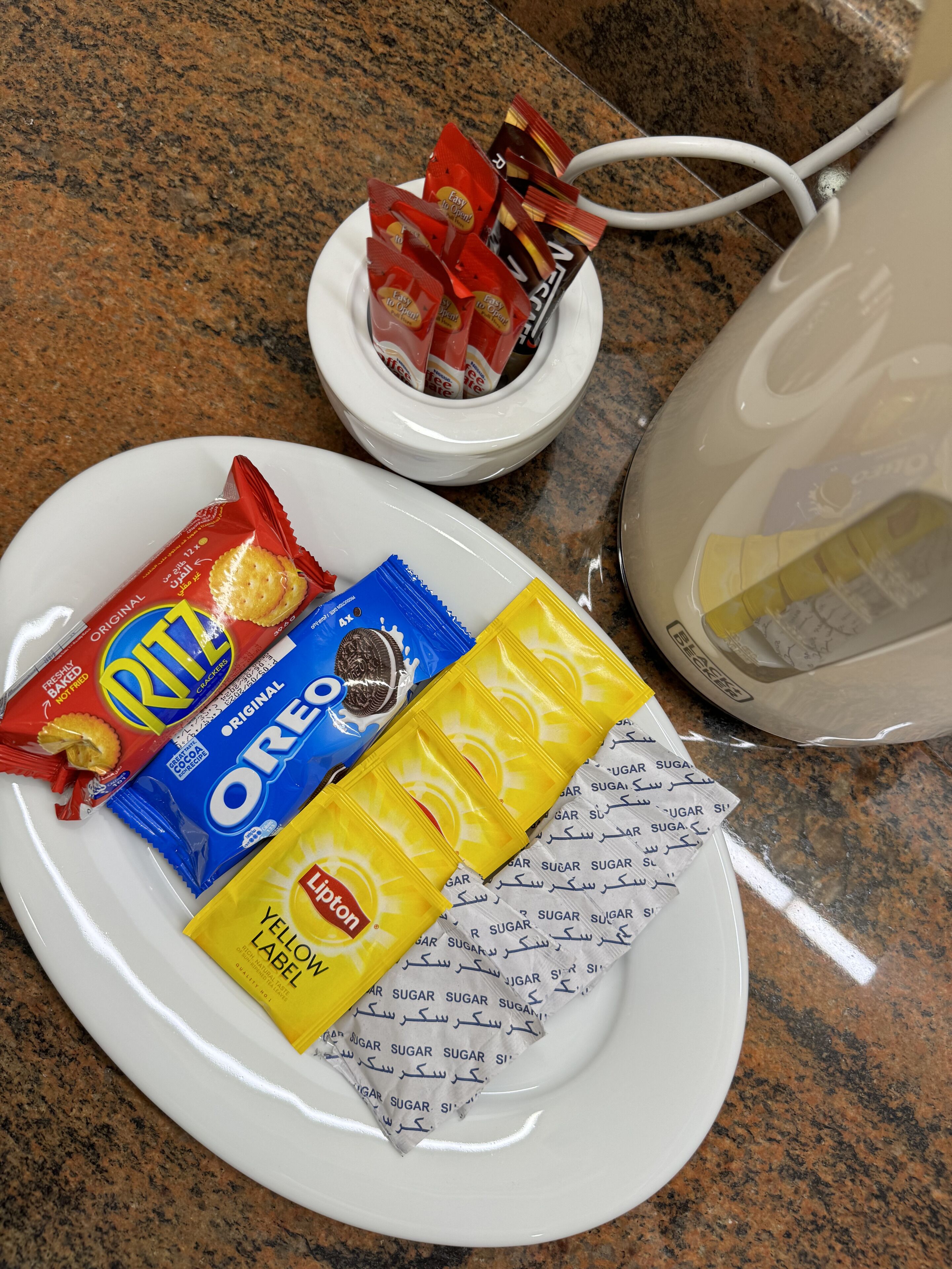 Un plato con galletas Ritz, Oreos y sobrecitos de azúcar amarillo sobre una encimera de granito.