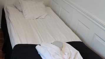 Una cama individual con ropa de cama blanca y un cabecero negro, una almohada blanca y una toalla blanca doblada sobre la cama.
