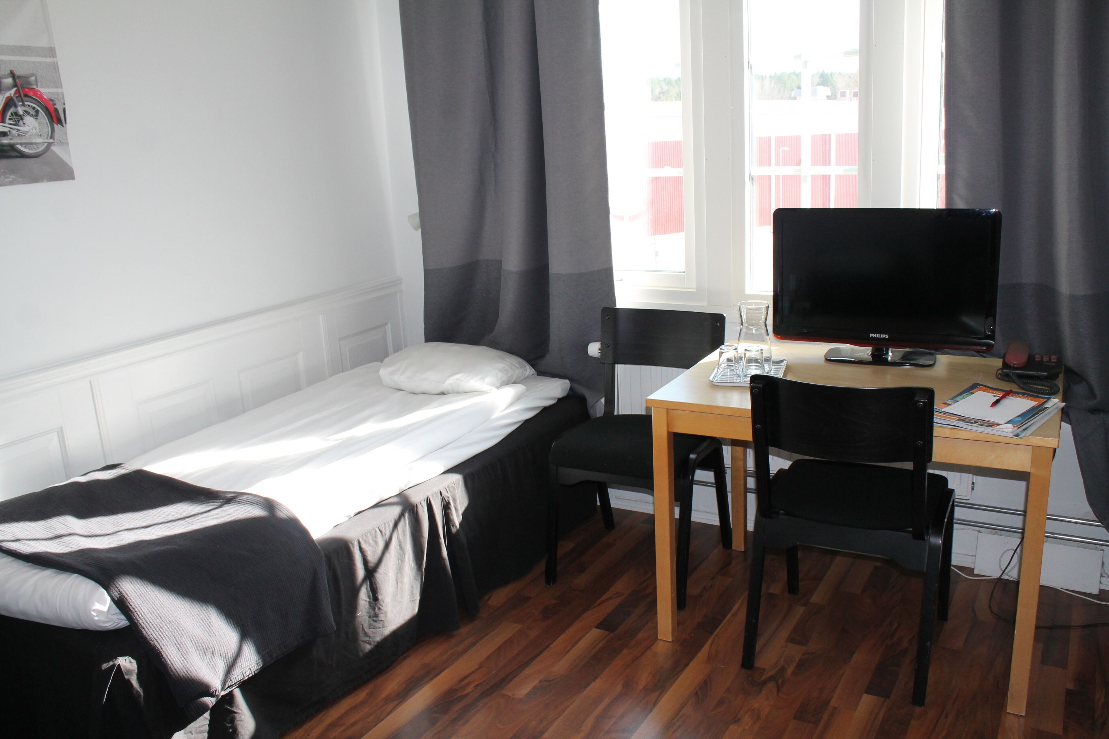 Una habitación pequeña y ordenada con una cama individual, un escritorio con un ordenador y una silla.