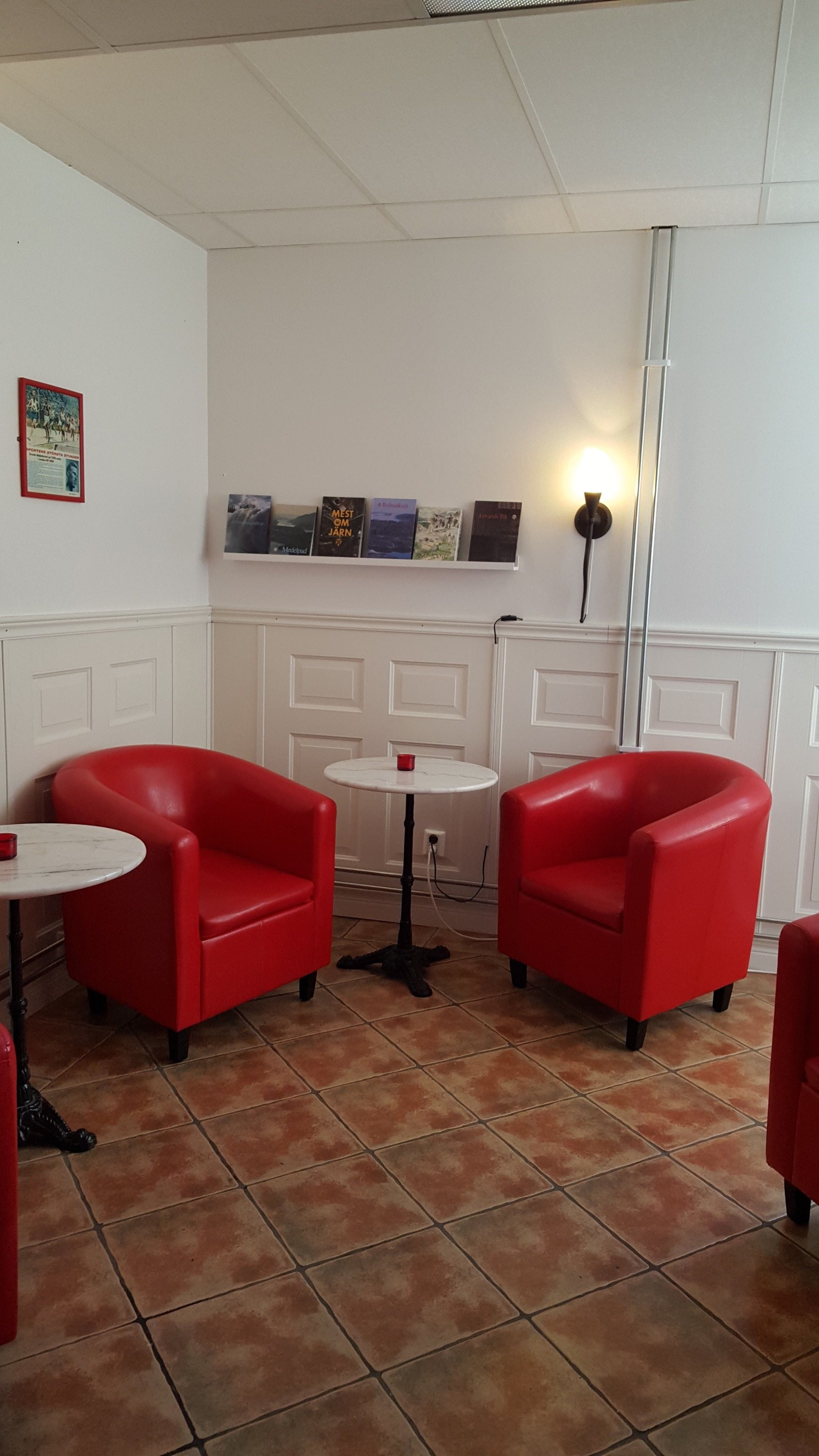 A room with two red armchairs, a small white table, and a shelf with books.