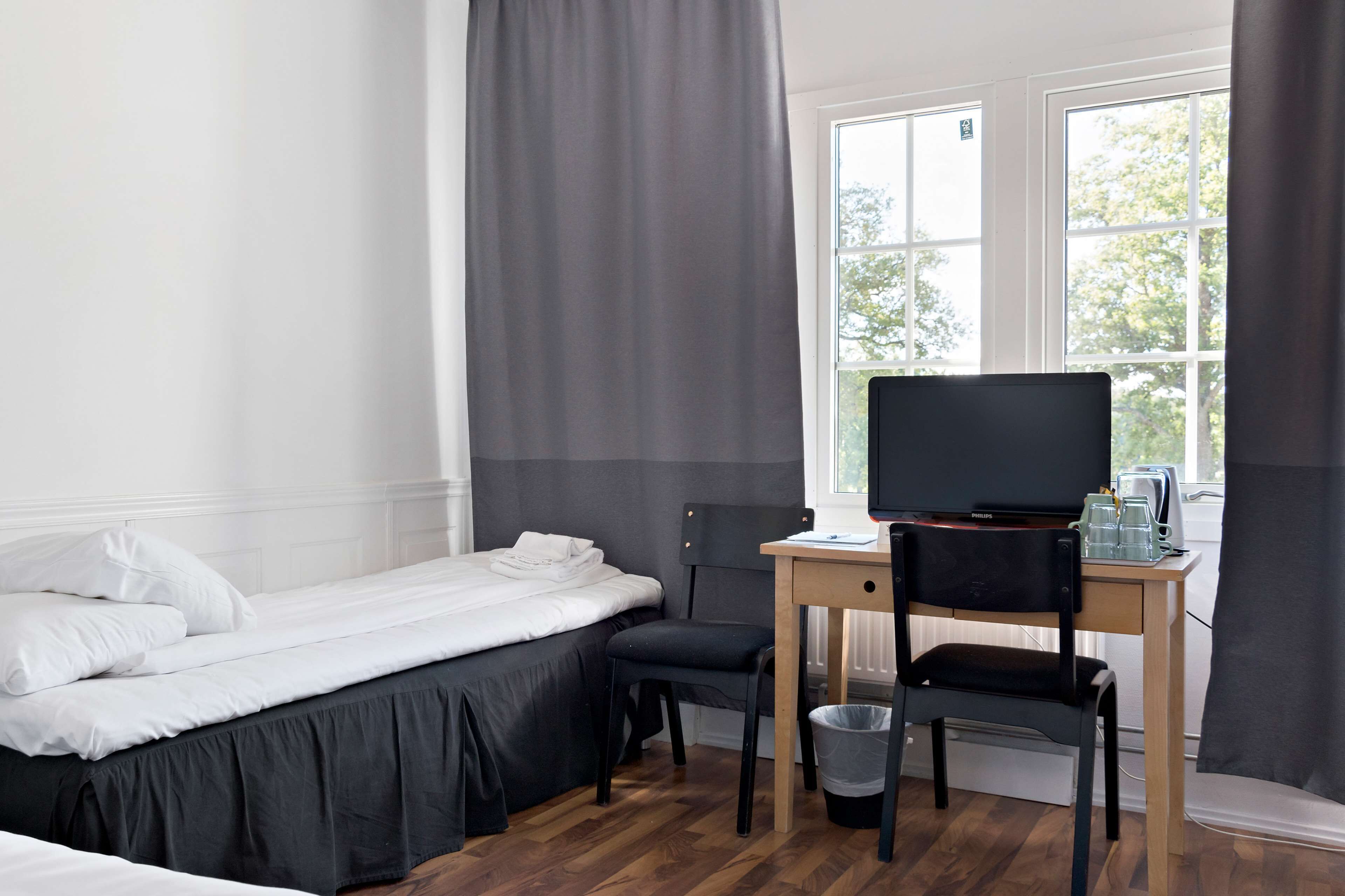 A hotel room with a bed, a desk with a computer and a television, a chair, and a window with curtains.