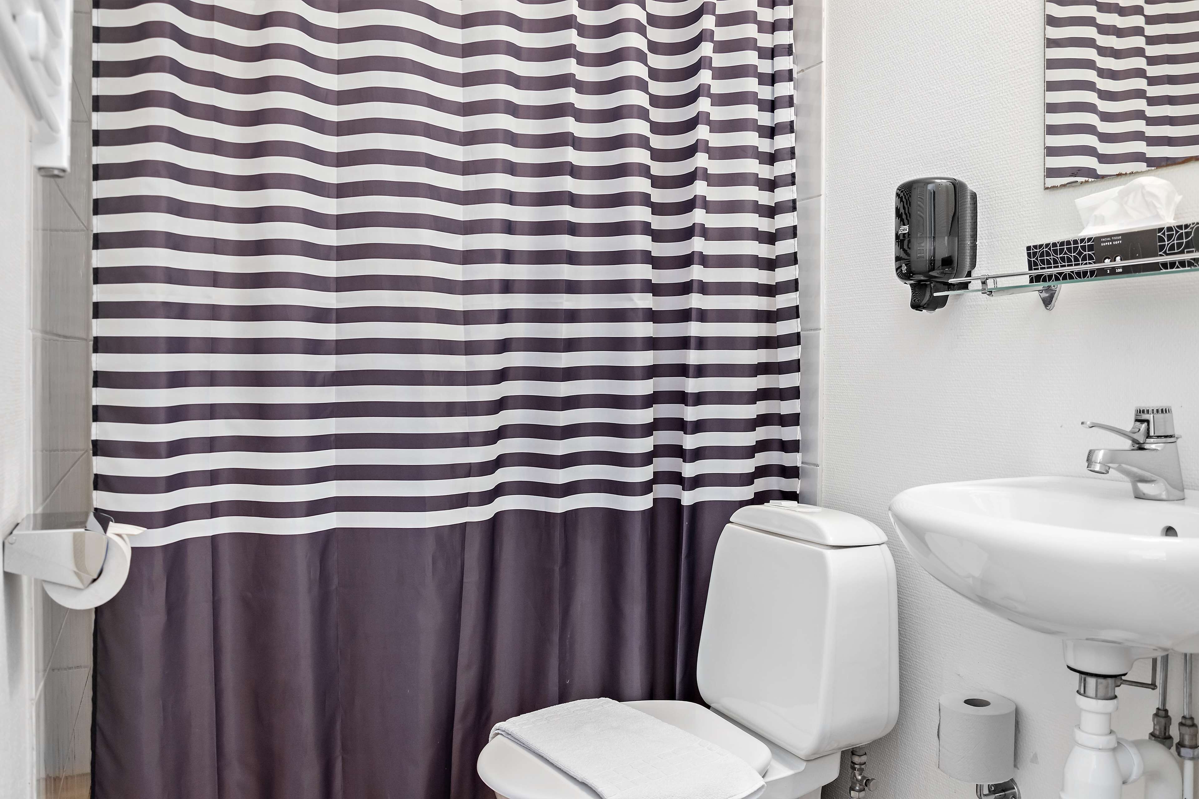Un baño con cortina de ducha a rayas, un lavabo blanco y un inodoro.