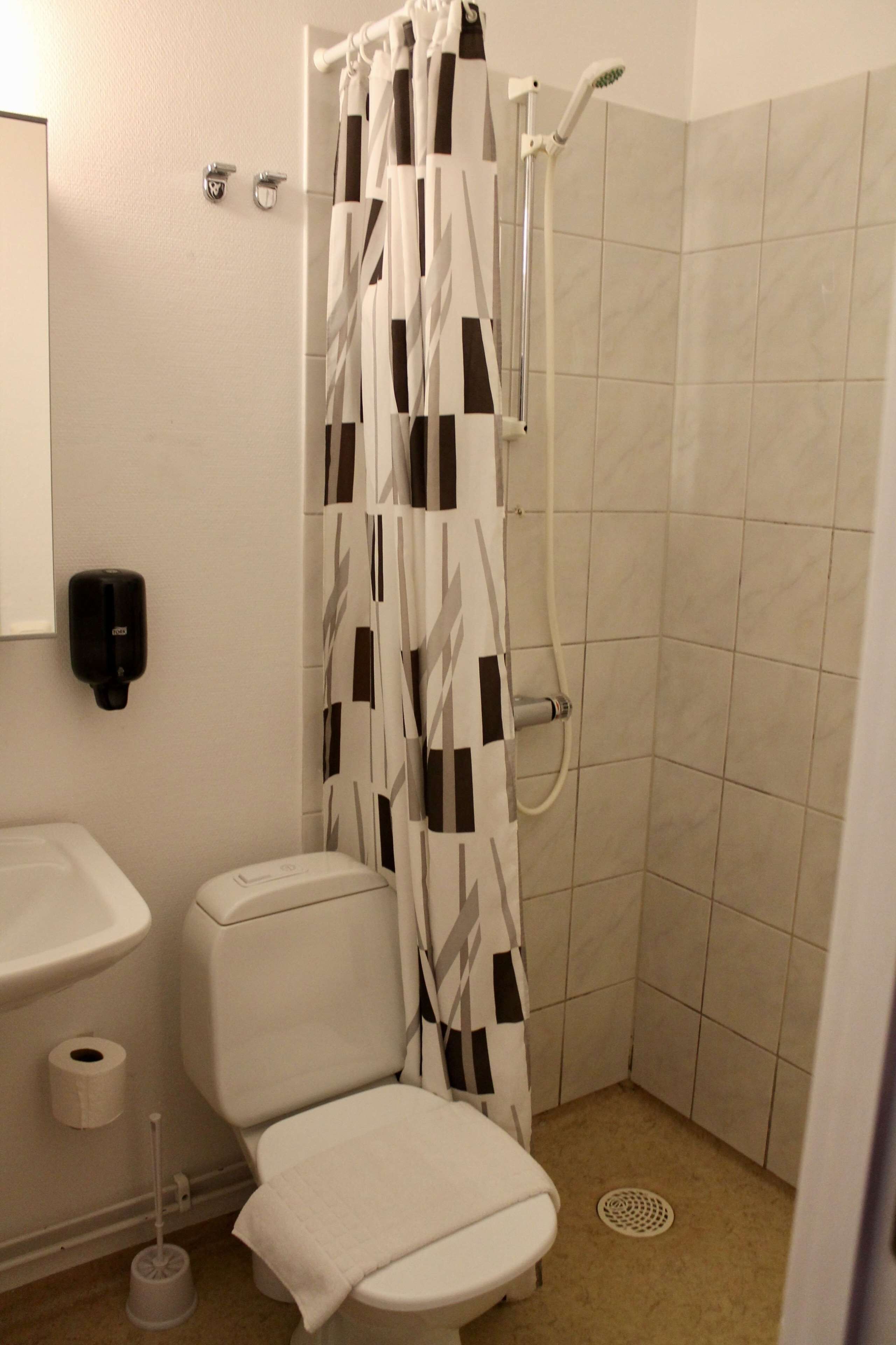A bathroom with a toilet, sink, shower, and hand dryer.