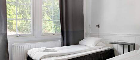 Una habitación de hotel con dos camas, una ventana con cortinas, un radiador y una mesita pequeña.