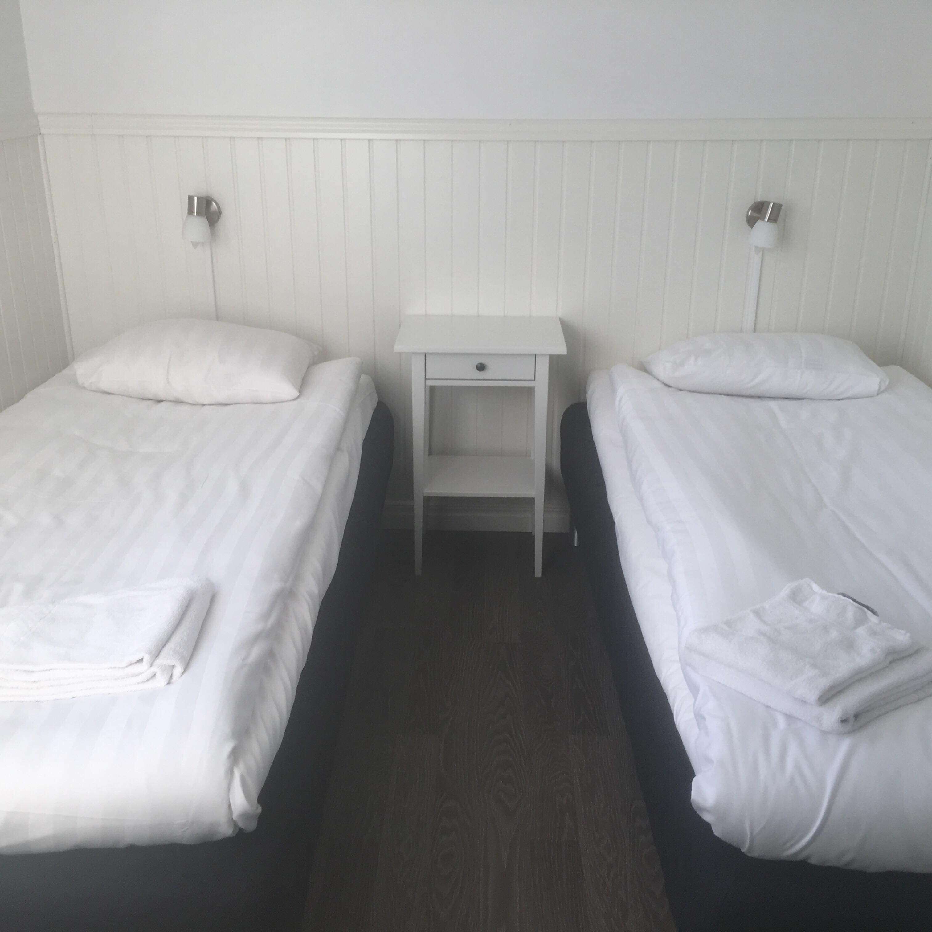 A hotel room with two single beds, each with a pillow and a folded towel.