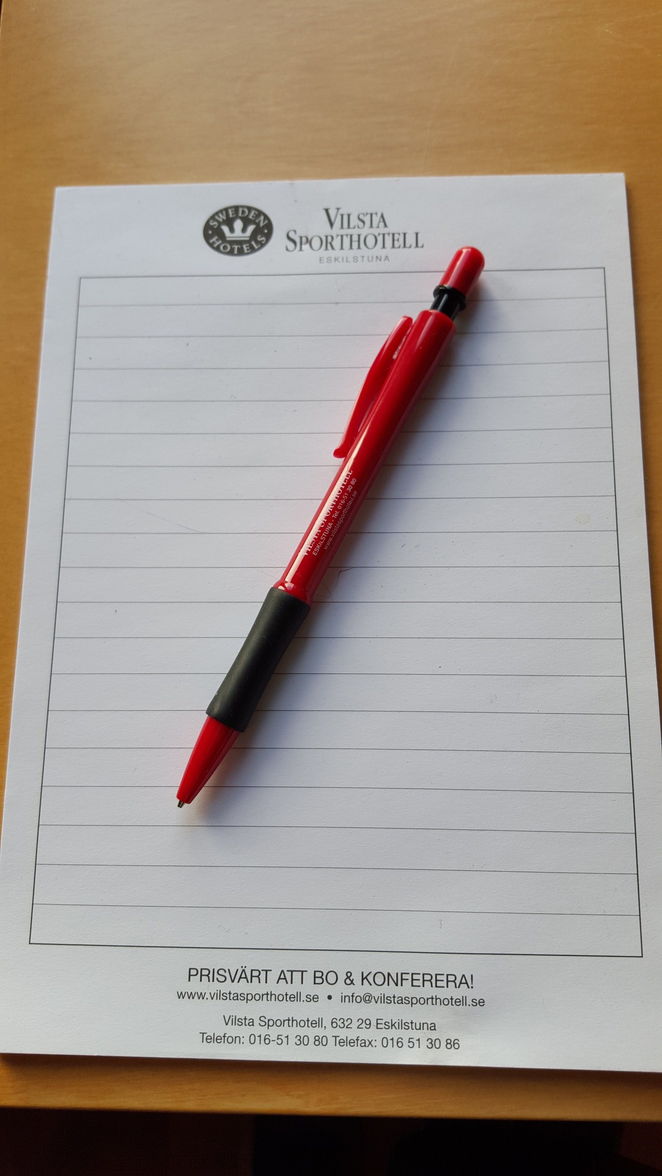 Una pluma roja sobre un papel cuadriculado con el logo y el nombre de Vilsta Sporthotell.