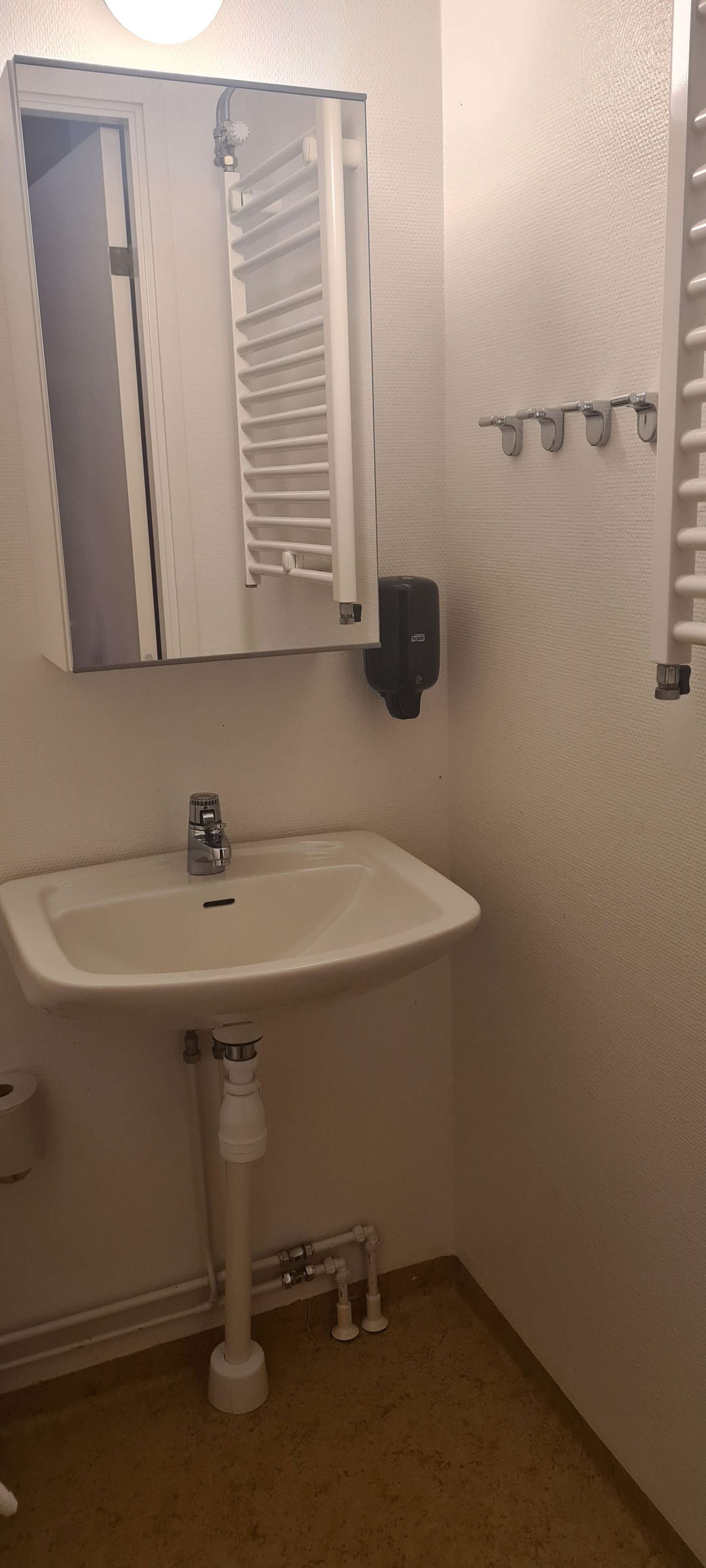 Une salle de bain avec un lavabo blanc, un miroir, un porte-serviettes et un distributeur de savon.