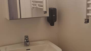 Une salle de bain avec un lavabo blanc, un miroir, un porte-serviettes et un distributeur de savon.