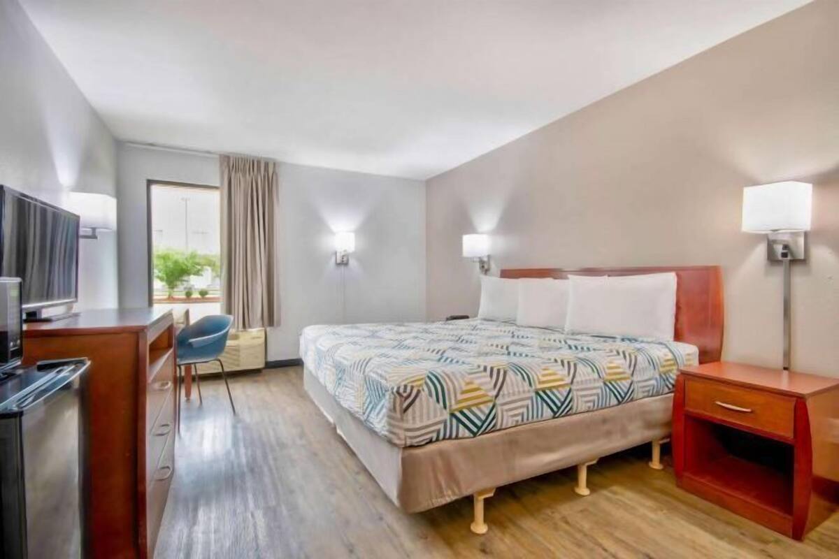 A hotel room with a bed, bedside tables, a desk, a chair, and a TV.