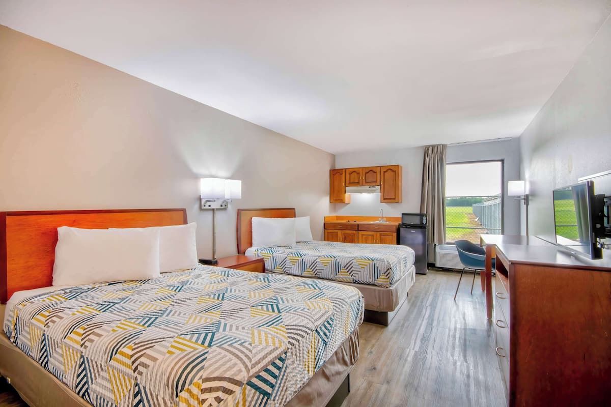 A hotel room with two beds, a desk, a chair, a TV, and a window with a view.