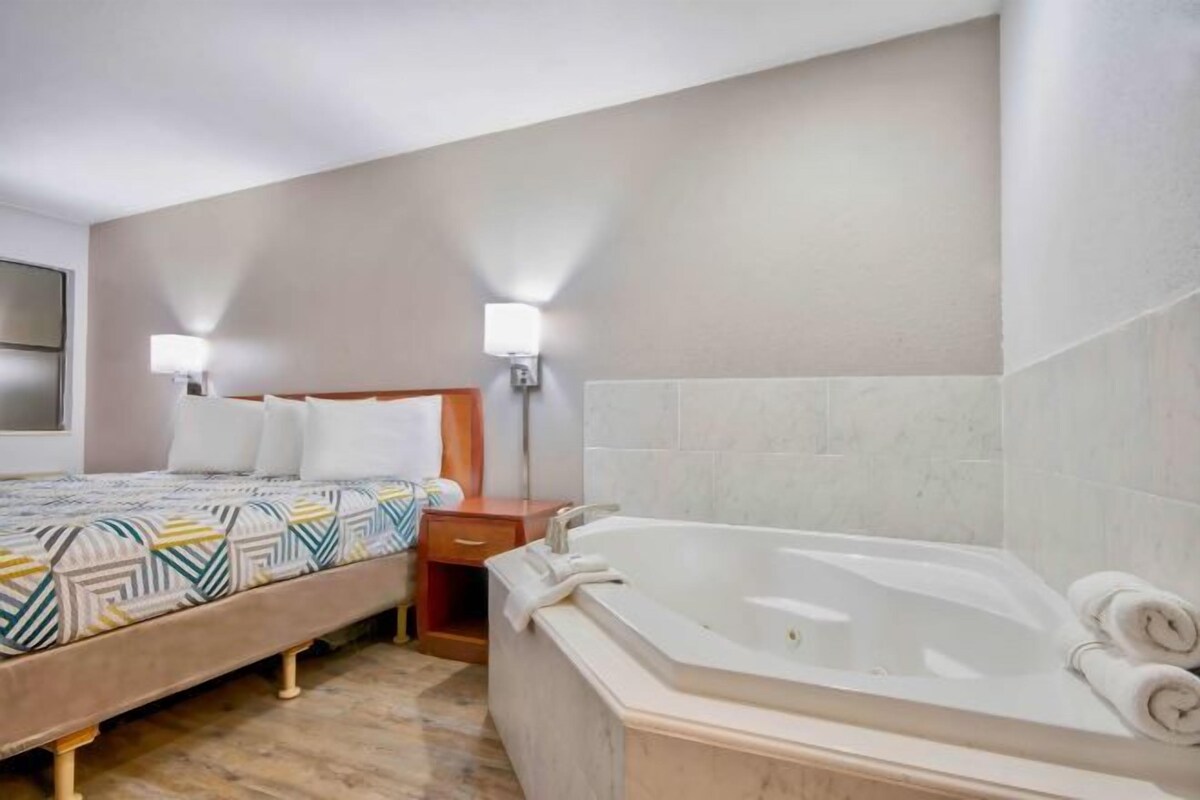 A hotel room with a bed, a large bathtub, and two wall-mounted lamps.