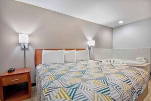 A hotel room with a bed, bedside table, lamp, and a bathroom with a bathtub and sink. - Motel 6 Abbeville, LA (Abbeville)