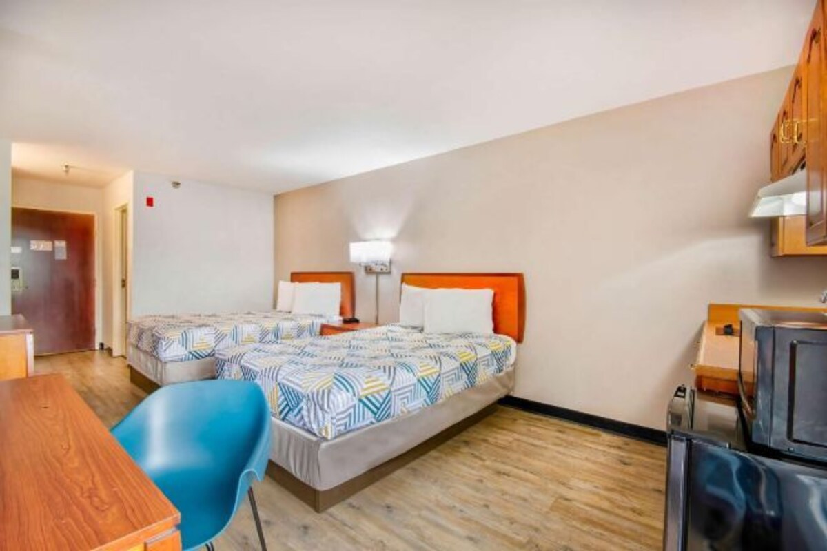 A hotel room with two beds, a desk, a chair, and a kitchenette.