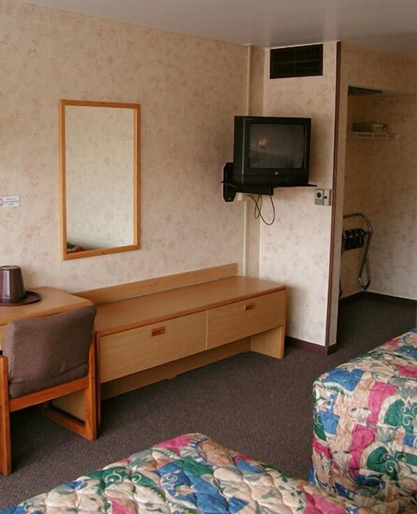 Una habitación pequeña y acogedora con un banco de madera, una cama individual con colcha colorida, un televisor montado en la pared y un espejo.