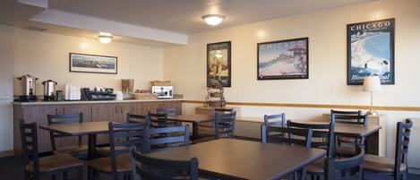 A restaurant with multiple tables and chairs, a counter with a coffee machine, and wall decorations including posters.