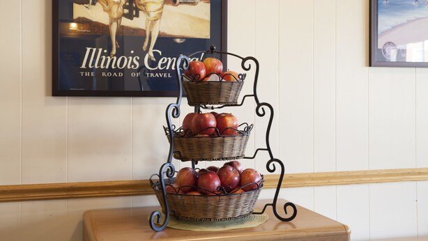 Un panier à fruits à trois niveaux, posé sur une table en bois, devant un mur orné de tableaux encadrés.