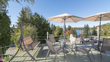 Terraza al aire libre con asientos y sombrillas, rodeada de árboles y vistas a un lago.