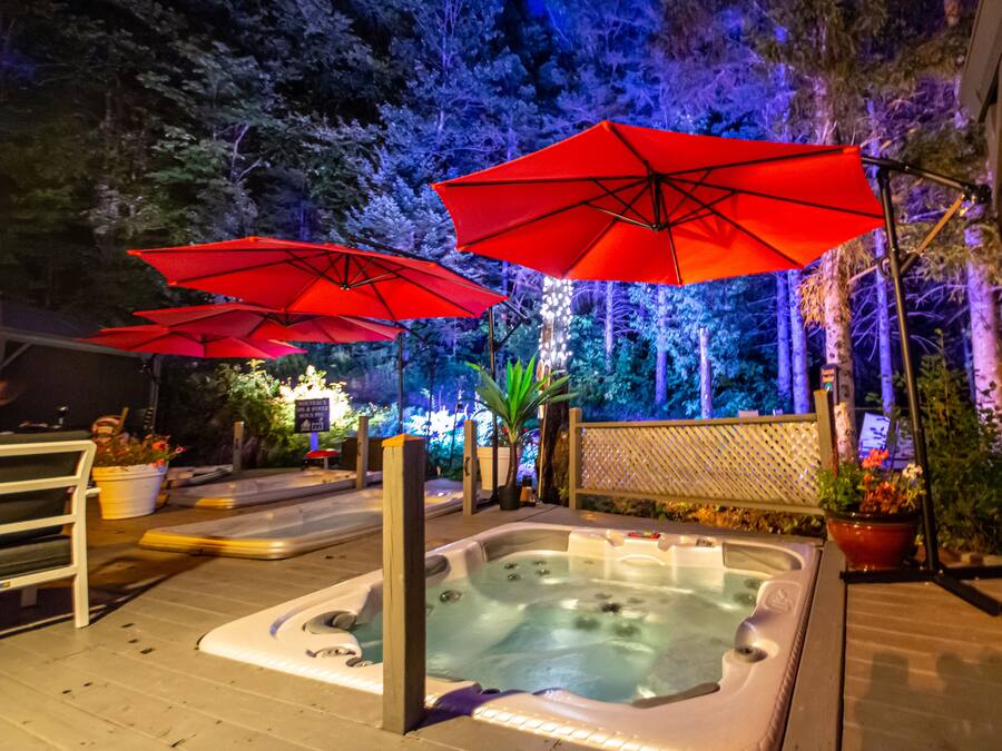 A hot tub area with red umbrellas, surrounded by trees and potted plants.