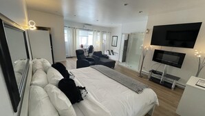 A modern hotel room with a large bed, a desk, a chair, a TV, and a shower area. - Auberge Hôtel Spa Watel (Sainte-Agathe-des-Monts)