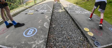 Una cancha de shuffleboard con una marca B y O, rodeada por una valla de madera y una zona cubierta de césped.