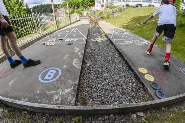 Una cancha de shuffleboard con una marca B y O, rodeada por una valla de madera y una zona cubierta de césped.