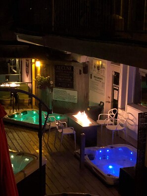 Terraza exterior con dos jacuzzis, piso de madera, sillas blancas y un cartel con texto en francés.