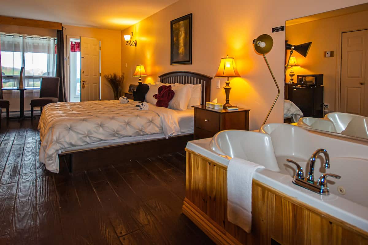 Een hotelkamer met twee bedden, een zithoek met een fauteuil, een groot bad en een spiegel.
