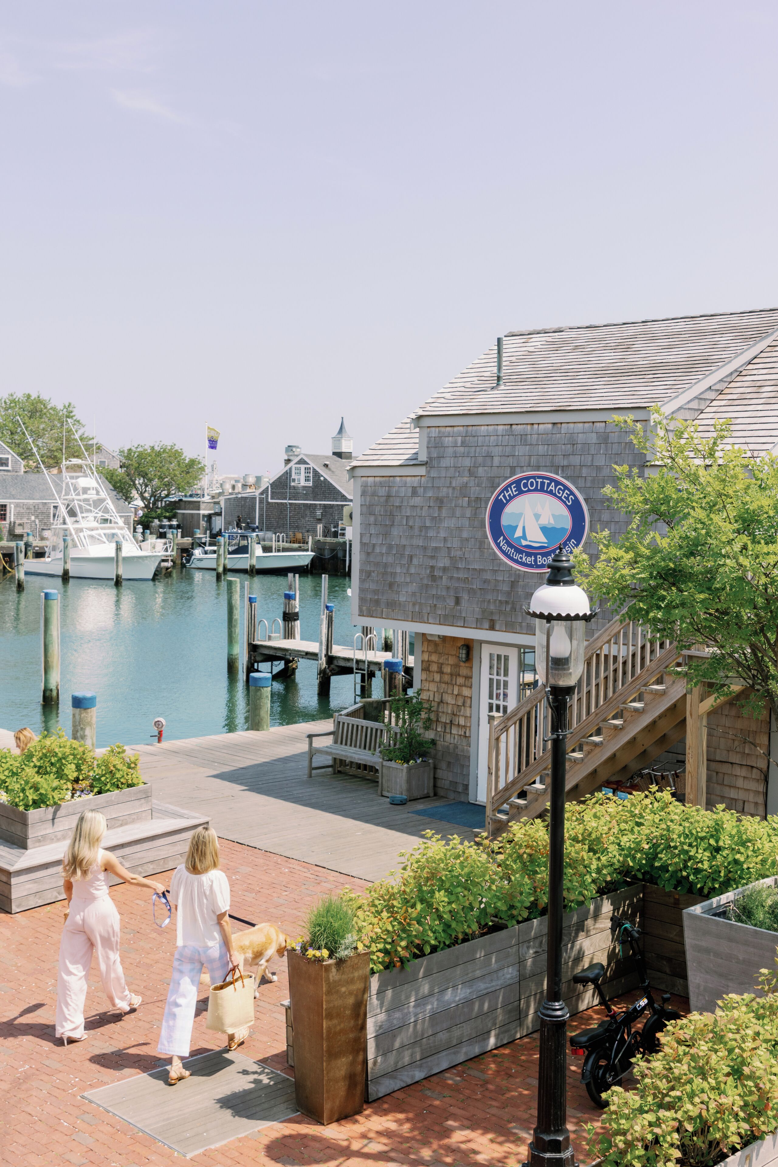 A waterfront property with a dock, a sign for 'The Cottages Nantucket Boat Haven,' and a staircase leading to a wooden deck.
