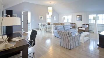 Un salón espacioso con techo alto, una zona de comedor con mesa y sillas, y un rincón acogedor con sofá y sillones.