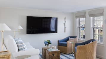 A modern living room with a large flat-screen TV, a white sofa, a blue armchair, wicker furniture, and a striped rug.