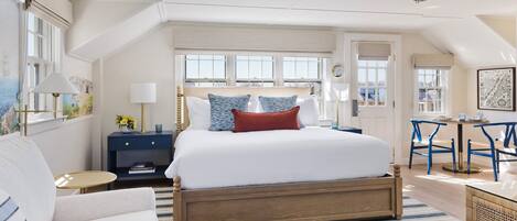 A bedroom with a large bed, a bedside table with a lamp, a chair, and a small table with a book and a decorative item.