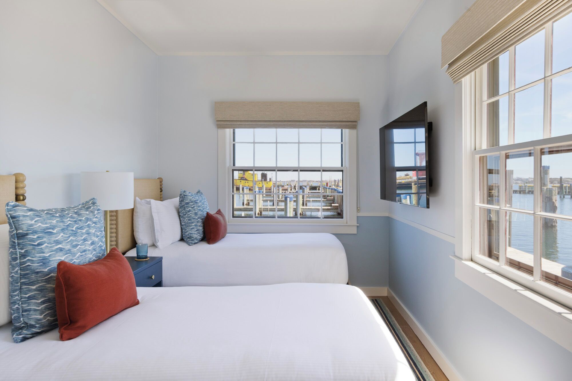 A hotel room with two beds, a large window with a view of a marina, and a mounted TV.