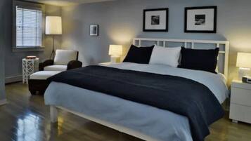 A modern bedroom with a large bed, bedside tables, a nightstand, a chair, and a window with blinds.