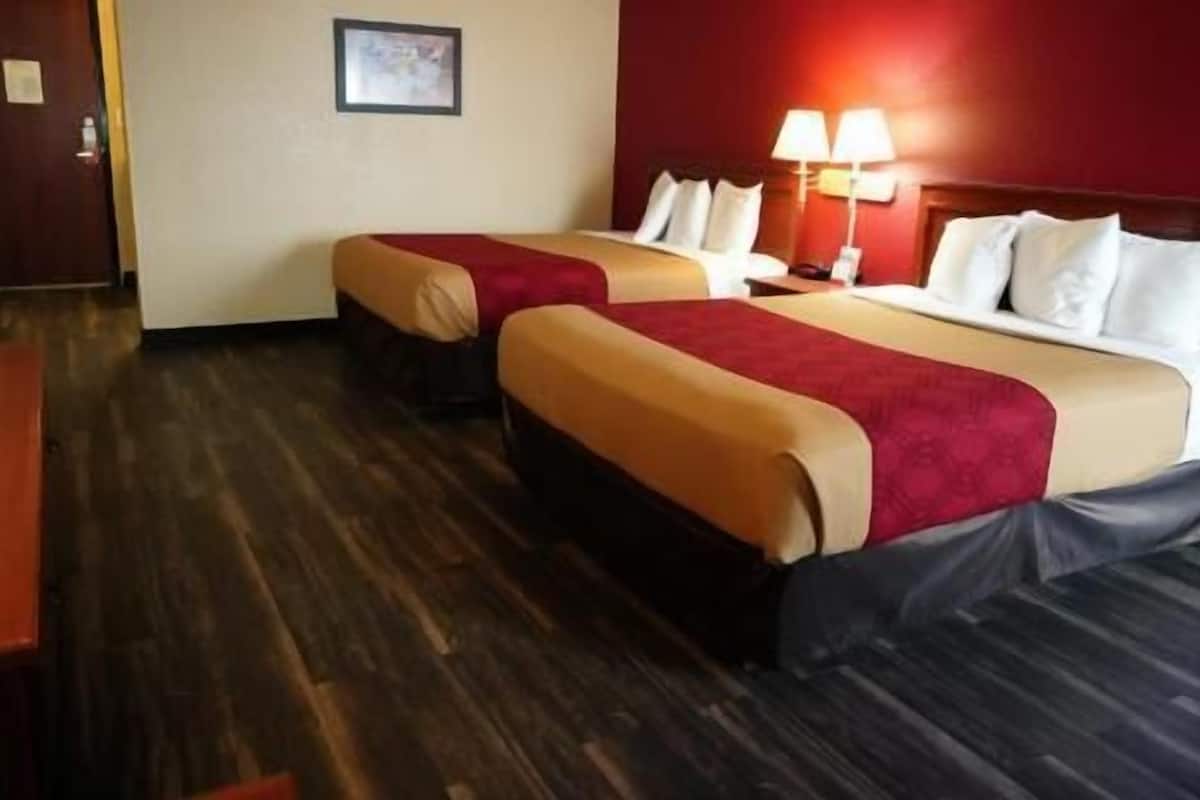 A hotel room with two beds, a wooden floor, a red wall, and a framed picture on the wall.