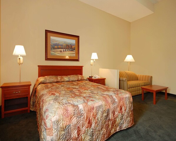 A hotel room with a large bed, two bedside tables, a chair, and a painting on the wall. - Econo Lodge Inn & Suites Kearney South (Kearney)