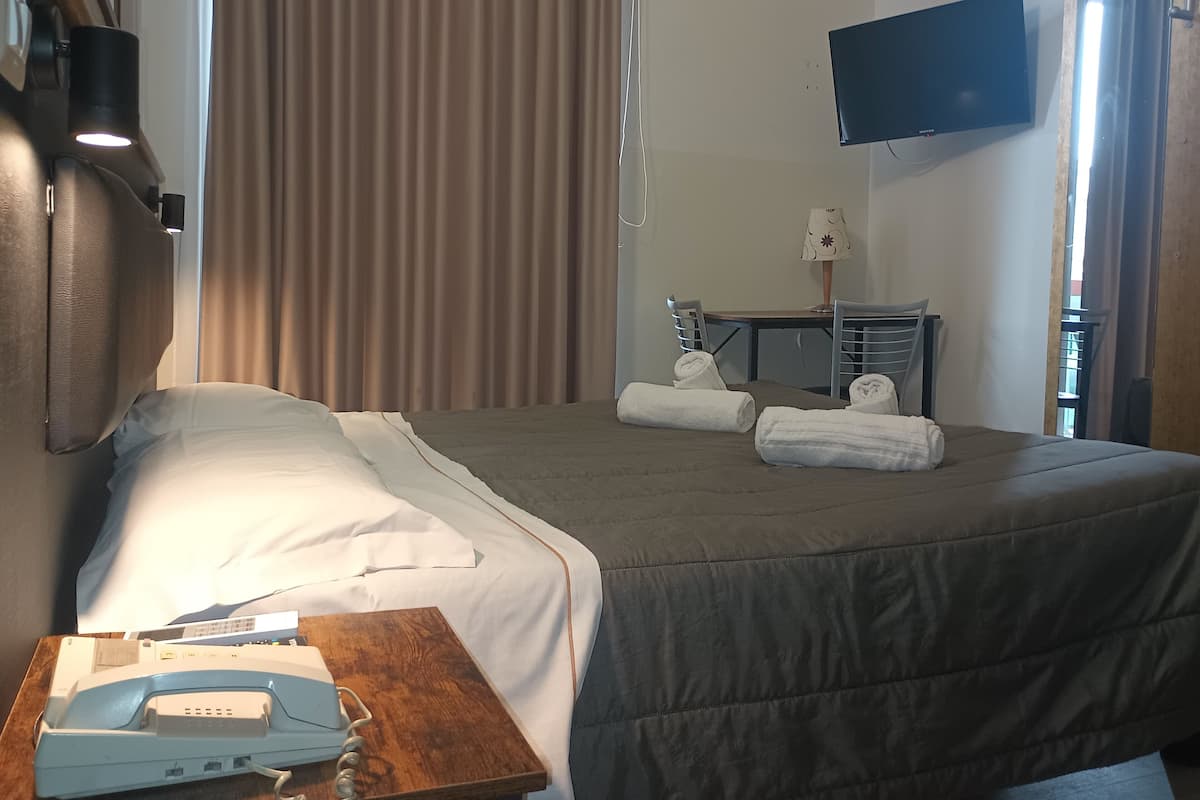 A hotel room with a bed, a desk with a telephone, a television mounted on the wall, and a window with curtains.