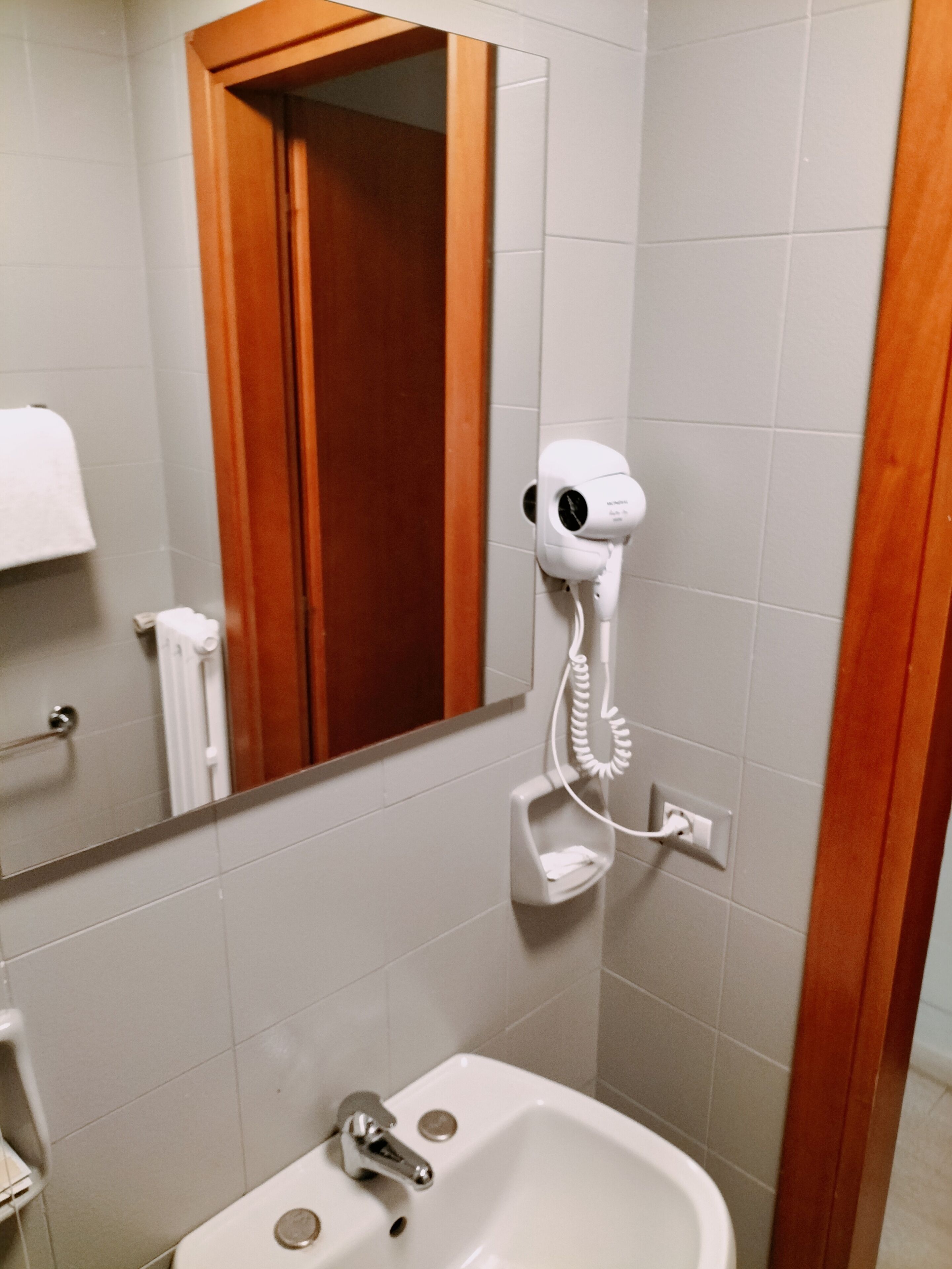 Ein Badezimmer mit einem weißen Waschbecken, einem Spiegel und einem an der Wand befestigten Föhn.