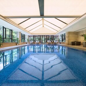 A large indoor swimming pool with clear blue water, surrounded by lounge chairs and a glass ceiling. - Zhejiang Xizi Hotel (Hangzhou)