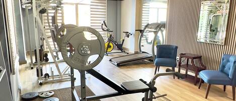 Un gimnasio con diferentes equipos de ejercicio, incluyendo una caminadora, bicicleta estática y zona de pesas.