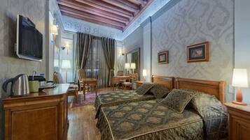 Habitación de hotel con dos camas, un escritorio, una silla, un televisor y una ventana con cortinas.