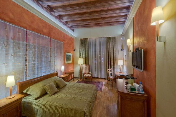 Una habitación de hotel con una cama grande, un escritorio con silla, televisión y ventana con cortinas.