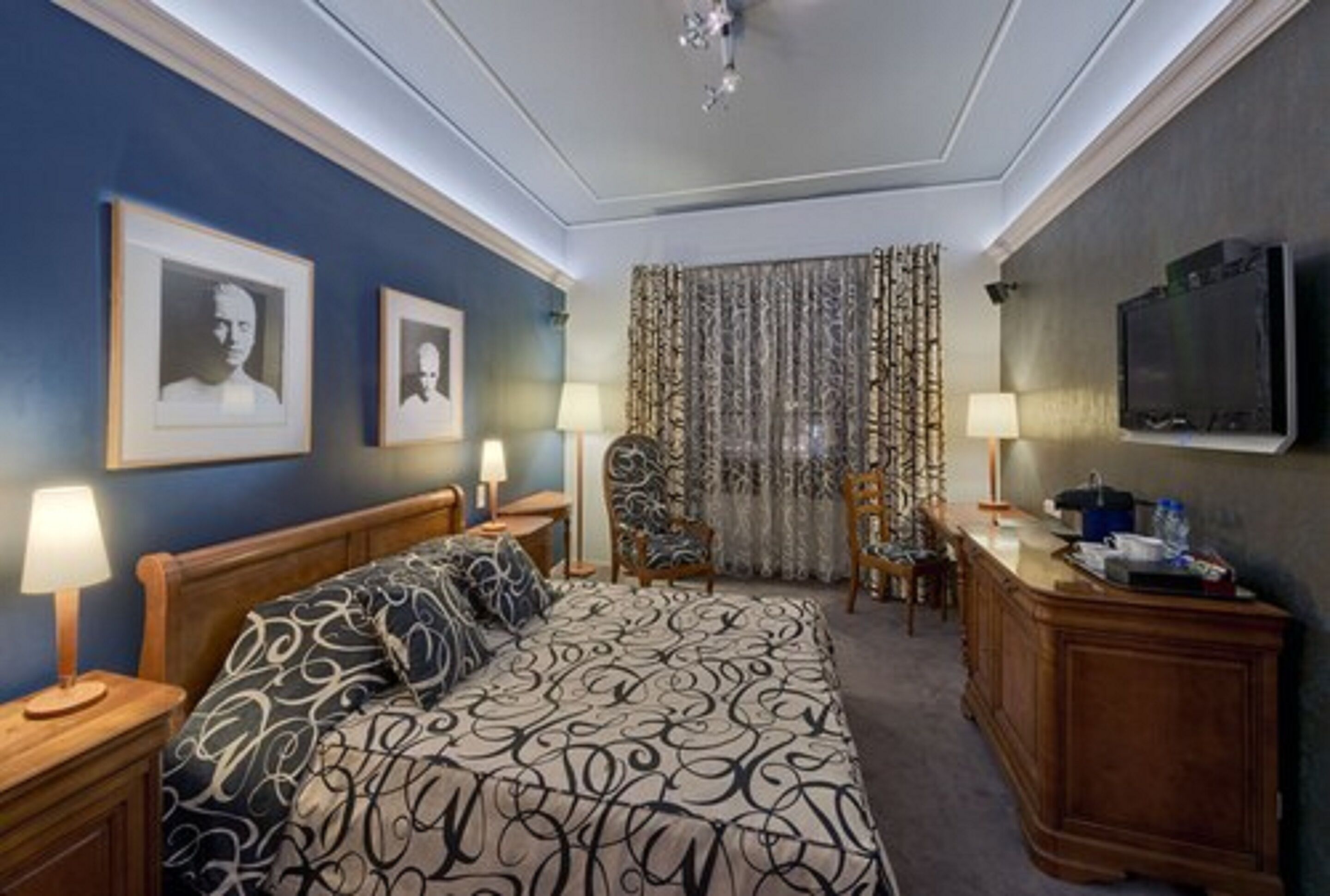 Una habitación de hotel con una cama grande, dos mesitas de noche con lámparas, un escritorio con televisor y una silla.