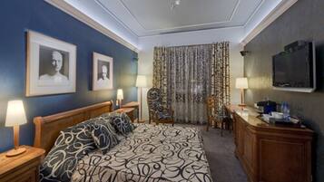 Una habitación de hotel con una cama grande, dos mesitas de noche con lámparas, un escritorio con televisor y una silla.
