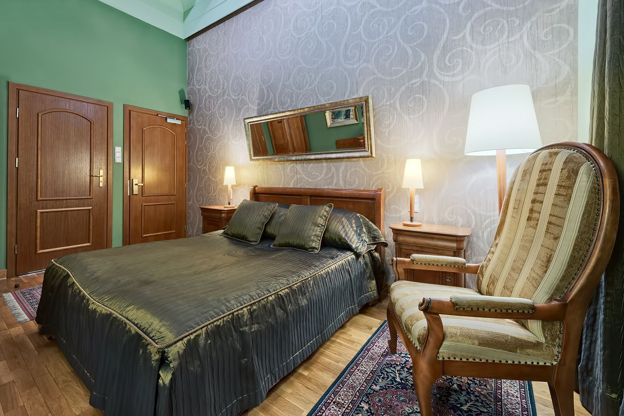 Quarto de hotel com uma cama grande, duas mesas de cabeceira, uma cadeira, um espelho e parede estampada.