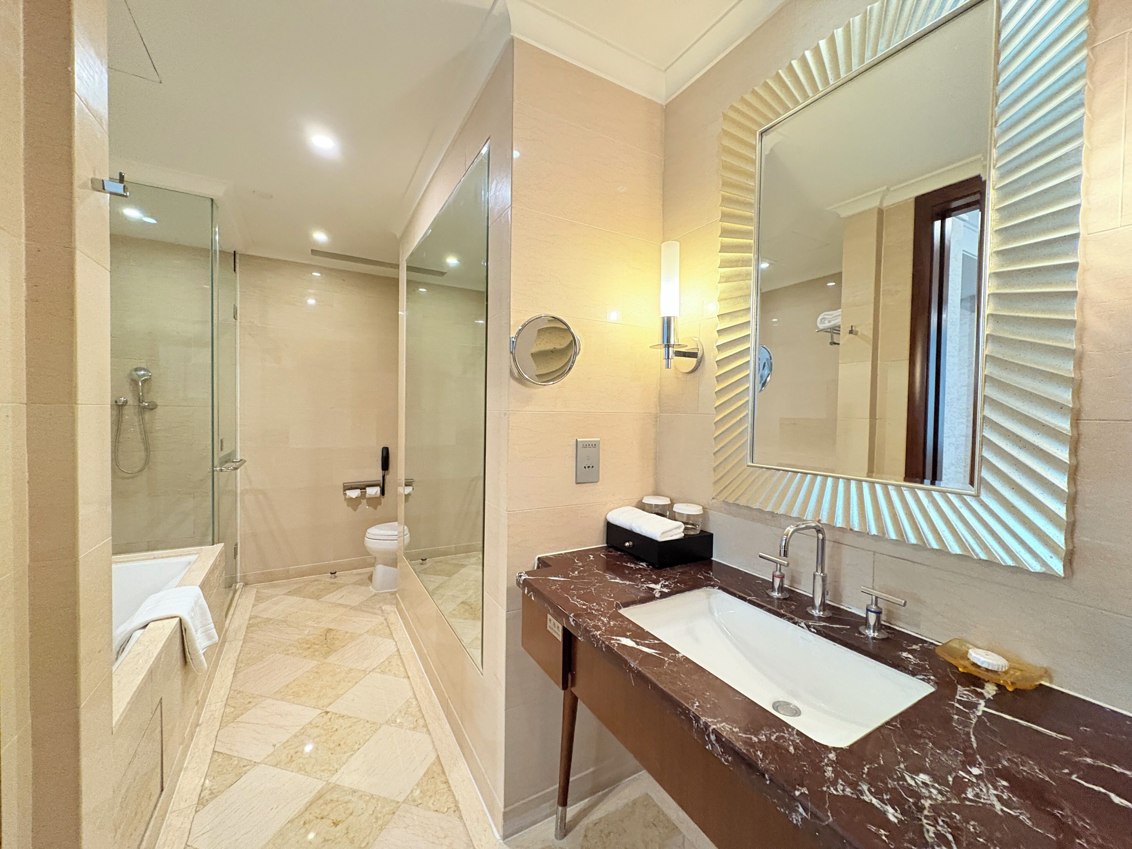 A modern bathroom with a glass-enclosed shower, a marble sink, and a large mirror with a unique frame.