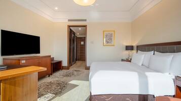 A hotel room with a large bed, a flat-screen TV, a wooden desk, and a door leading to a hallway.