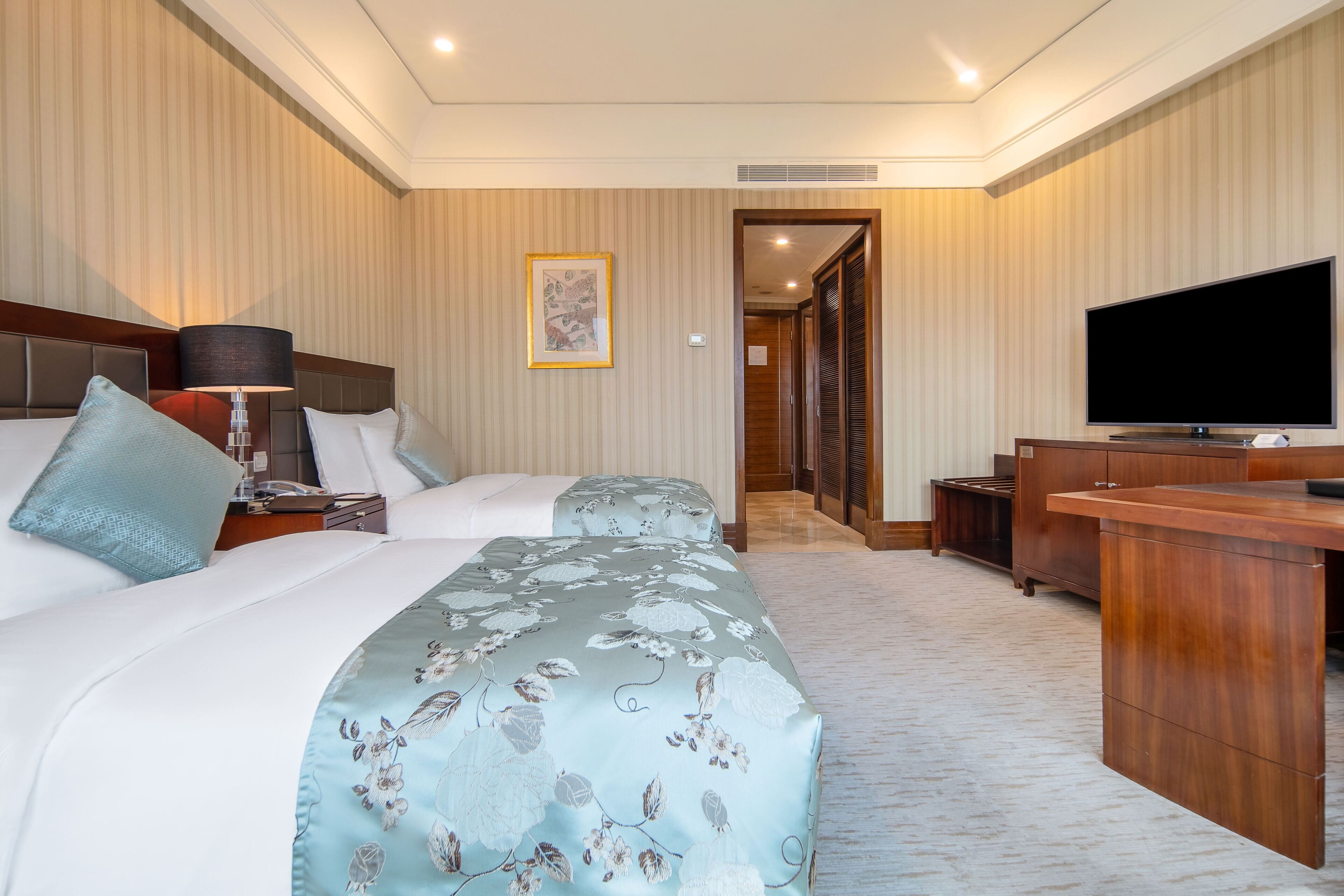 A hotel room with a bed, a desk, a television, and a framed picture on the wall.