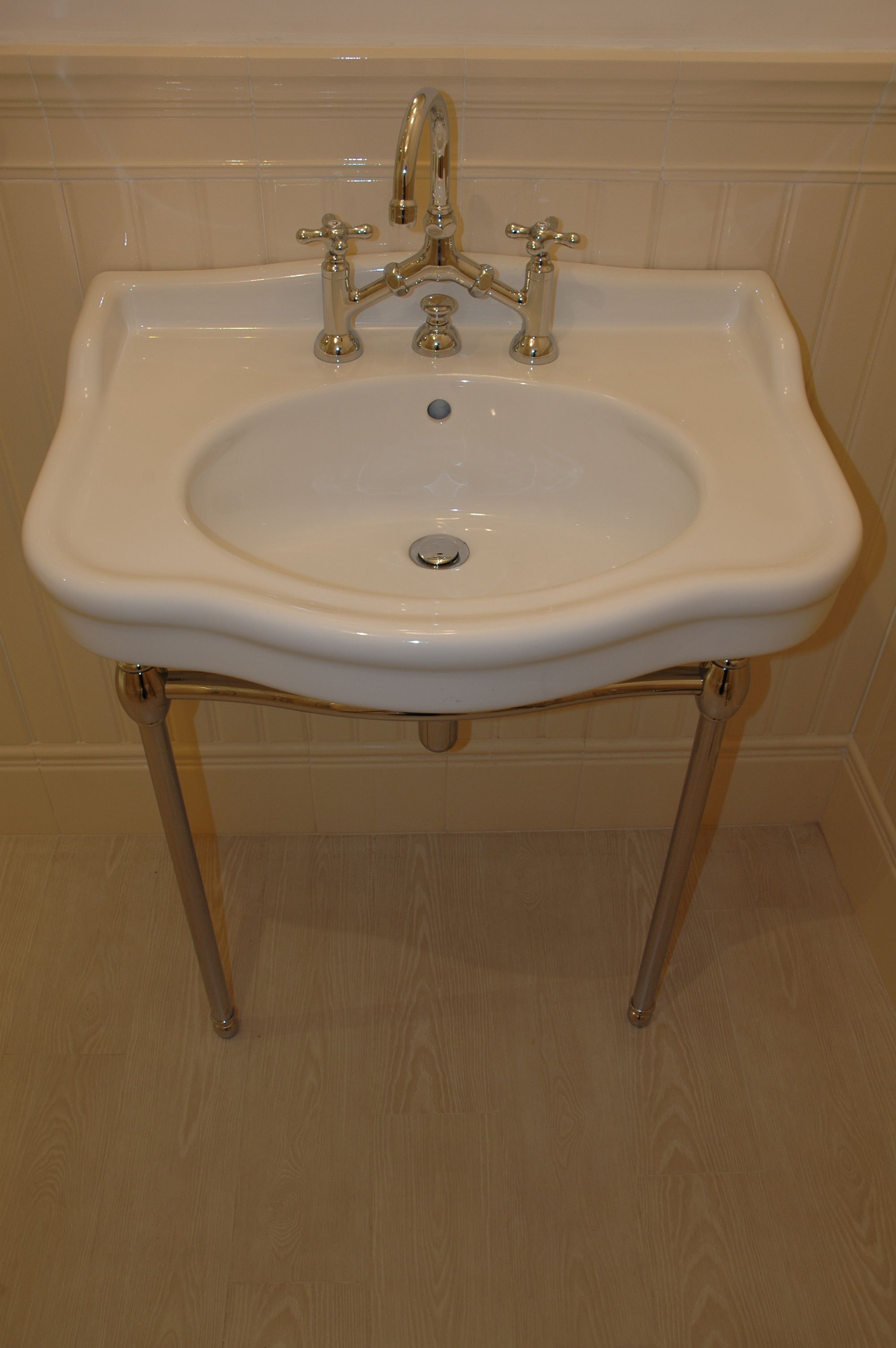 A white pedestal sink with two faucets and a drain.