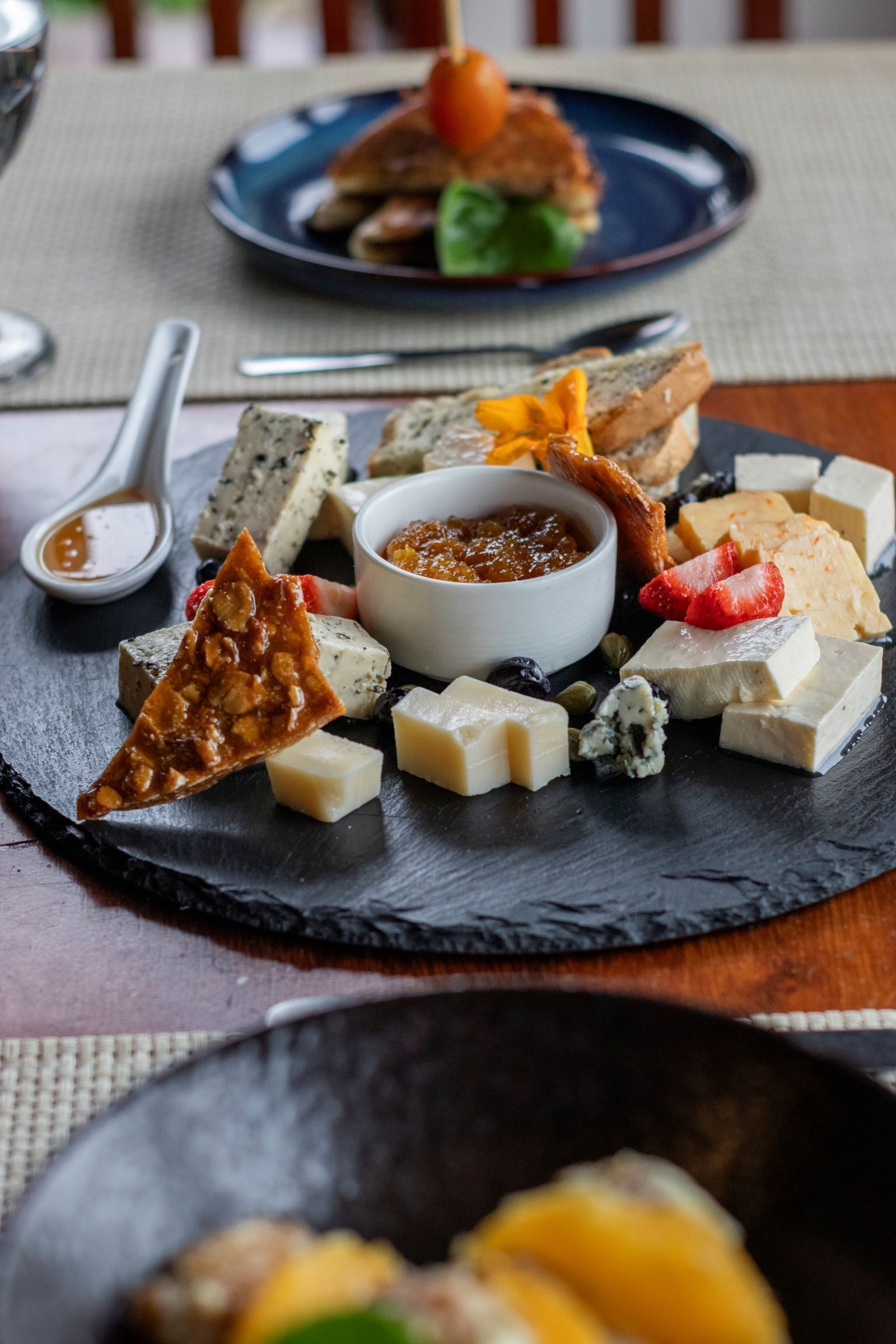 Una variedad de quesos y frutas sobre una tabla de pizarra, con un recipiente de chutney y una cuchara.